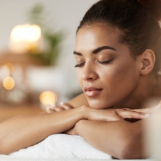 Serene woman with eyes closed enjoying a spa treatment, resting on a massage table with a peaceful expression, surrounded by soft, blurred candlelight, in a calm and soothing environment designed for relaxation and self-care