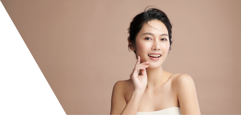Smiling young woman with a radiant expression and medium-length dark hair styled in soft waves, with strands delicately framing her face. Her glowing and flawless skin enhances her youthful appearance. She wears a simple, strapless top, contributing to the clean and elegant vibe. One hand is raised to her face, gently touching her cheek, while she smiles directly at the camera, creating an inviting and engaging look. The background features a soft, warm beige color that complements her skin tone, with a sleek black triangle on the left adding a modern design element. The overall feel of the image conveys beauty, confidence, and sophistication.