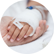 Two hands gently clasped together, conveying a sense of comfort and support. The larger hand appears to be an adult's, offering a warm, nurturing grip, while the smaller hand belongs to a child, who has a medical IV bandage wrapped around their wrist, indicating they are receiving treatment. The softly blurred background focuses attention on the hands, emphasizing their connection and the caring gesture involved. The overall mood of the image is tender and reassuring, highlighting the importance of care and compassion in a medical setting.