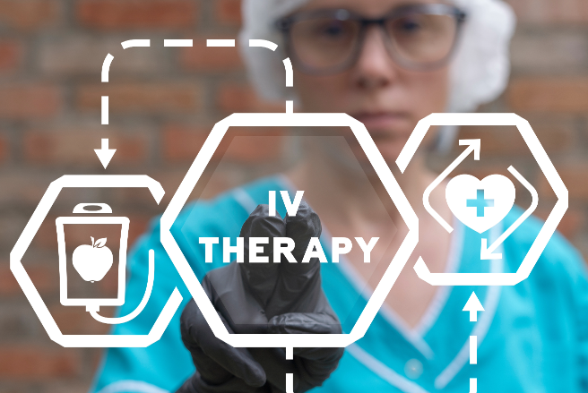 Healthcare professional wearing a light blue medical uniform and a white surgical cap, holding a gloved hand up as if pointing or gesturing toward graphic elements in the foreground. The central focus is on the text 'IV THERAPY' within a hexagonal shape, highlighting intravenous treatment. Surrounding this text are various icons and arrows: a hexagon with a bag (or container) and an apple, indicating the infusion of nutrients or hydration, and a heart icon with a plus sign, suggesting health improvement or vital signs. The background features a textured surface, likely brick, contrasting with the bright colors of the healthcare attire and graphics. The overall composition emphasizes the importance and benefits of IV therapy in a clinical setting