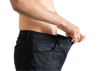 Close-up side profile of a man holding the waistband of oversized black pants, highlighting significant weight loss; bare upper body showcasing a toned physique against a plain background, emphasizing fitness transformation and body goals.